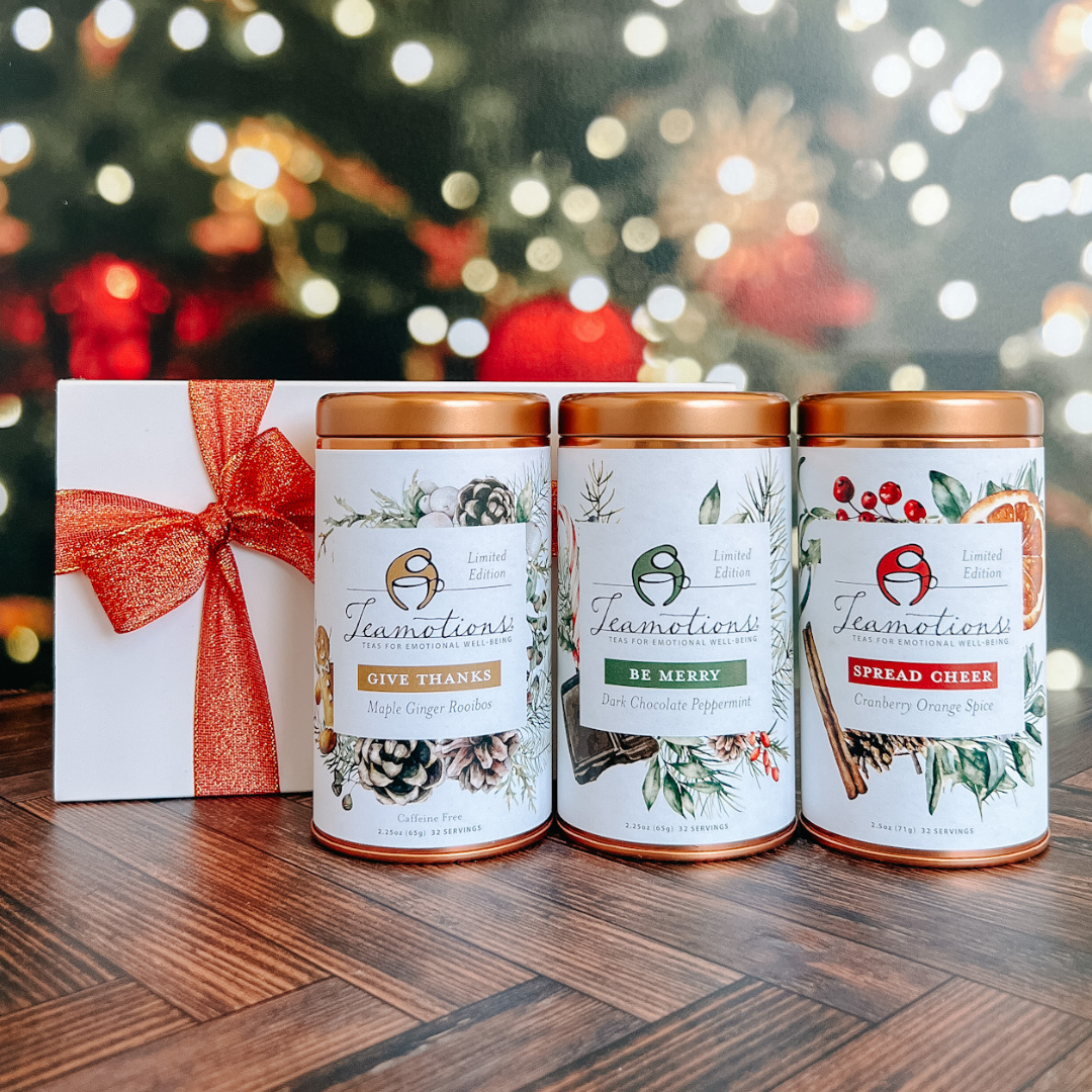 Three tea tins with holiday flavors, next to a gift box with a red ribbon.