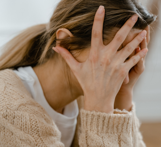 Person with hands covering face, wearing a beige sweater.