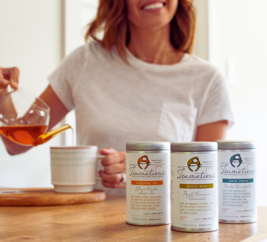 Person pouring tea with three tea canisters on a table.