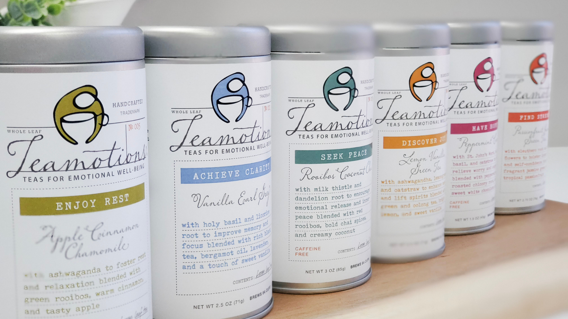 Six tins of Teamotions tea with different labels on a wooden surface.