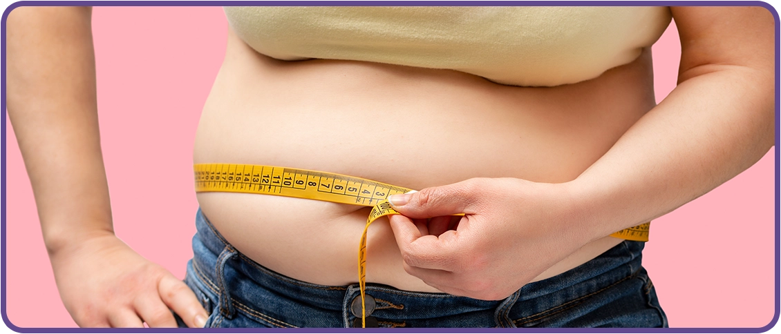 Person measuring waist with a yellow tape measure against a pink background.