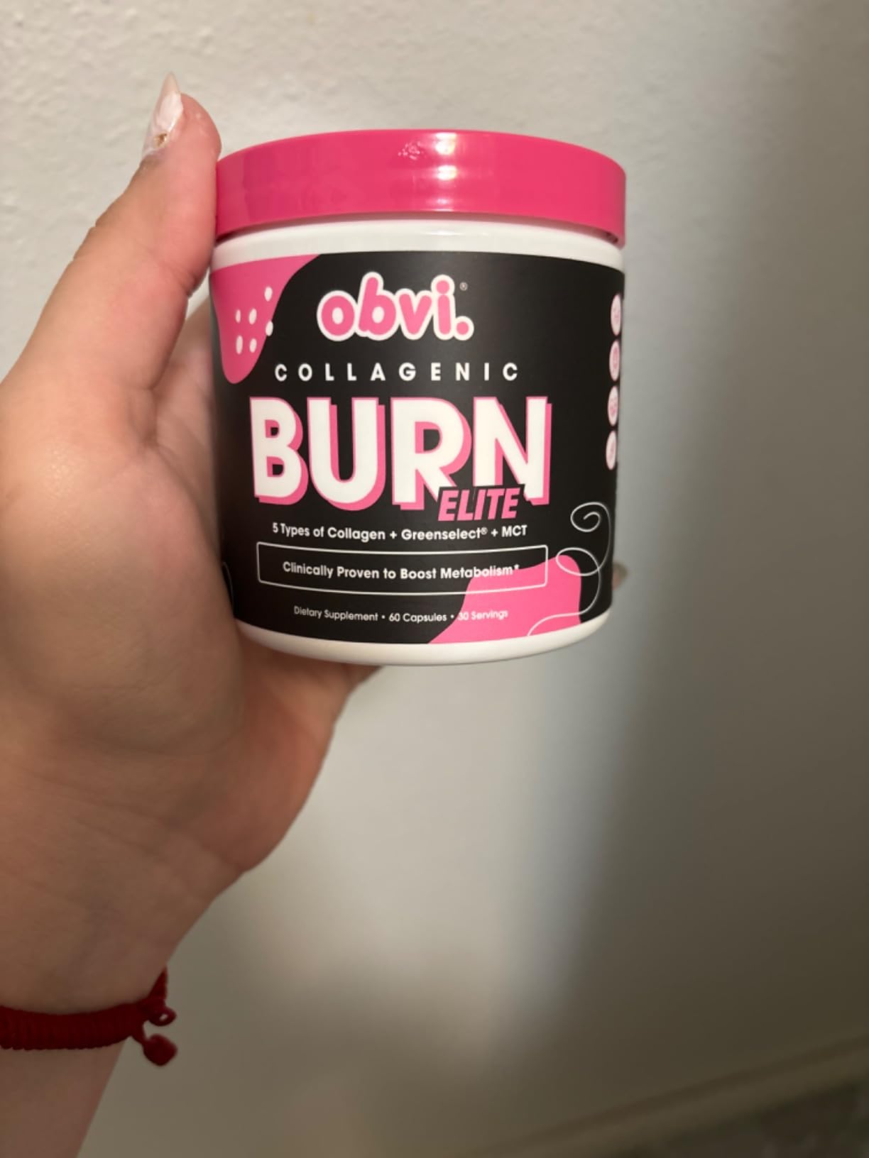 A hand holding a container of Obvi Collagenic Burn Elite supplements.