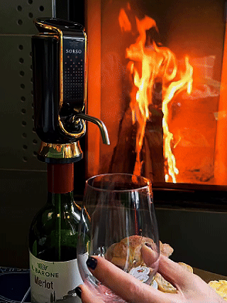 Wine being poured into a glass in front of a fireplace.