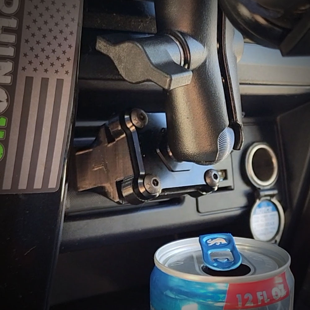A close-up of a black device mount installed in a vehicle's dashboard next to a power outlet.