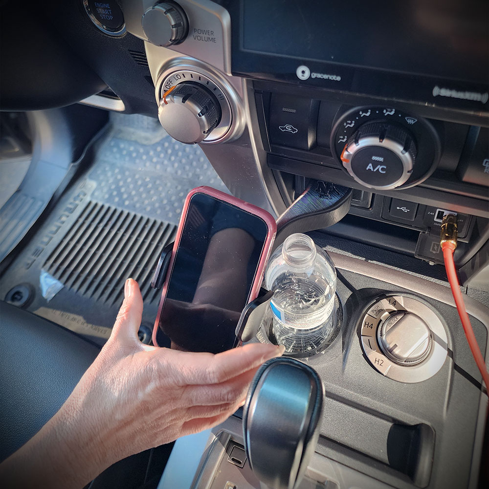 A hand adjusts a smartphone in a cupholder mount on a car's center console.