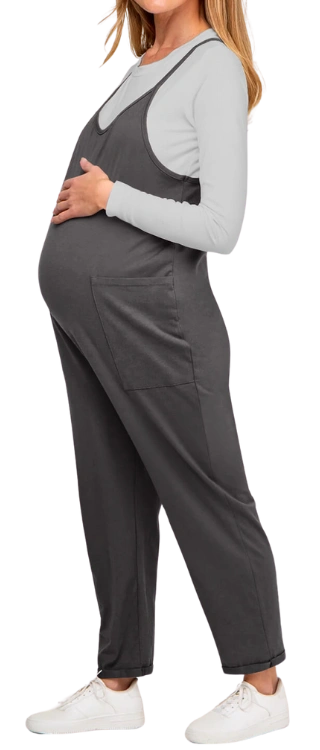 Pregnant woman in gray overalls and white sneakers, side view.