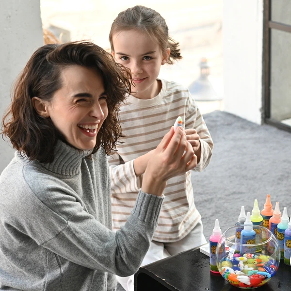 A woman and a child happily making colorful crafts together.