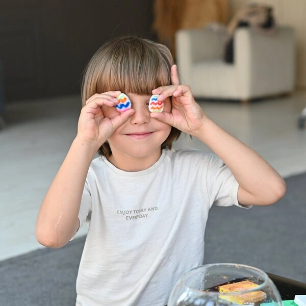 Child playfully holding cookies shaped like Easter eggs over eyes.