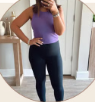 Person in purple top and black leggings taking a mirror selfie in a room.