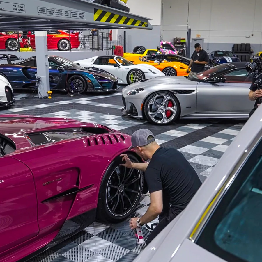 Multiple luxury cars in a garage with people cleaning them.