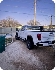 White pickup truck parked in a gravel driveway under a clear sky.