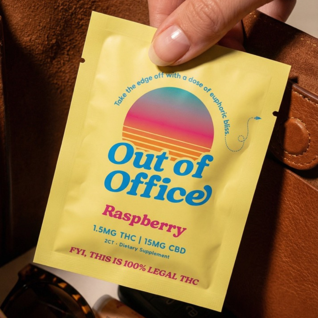 A hand holds a yellow packet of Out of Office Raspberry dietary supplement over a brown bag.