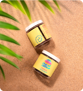 Two jars with yellow labels on sand, next to green leaves.
