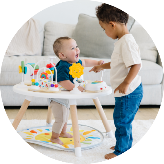 A toddler interacts with a smiling baby standing in a white and wood activity center.