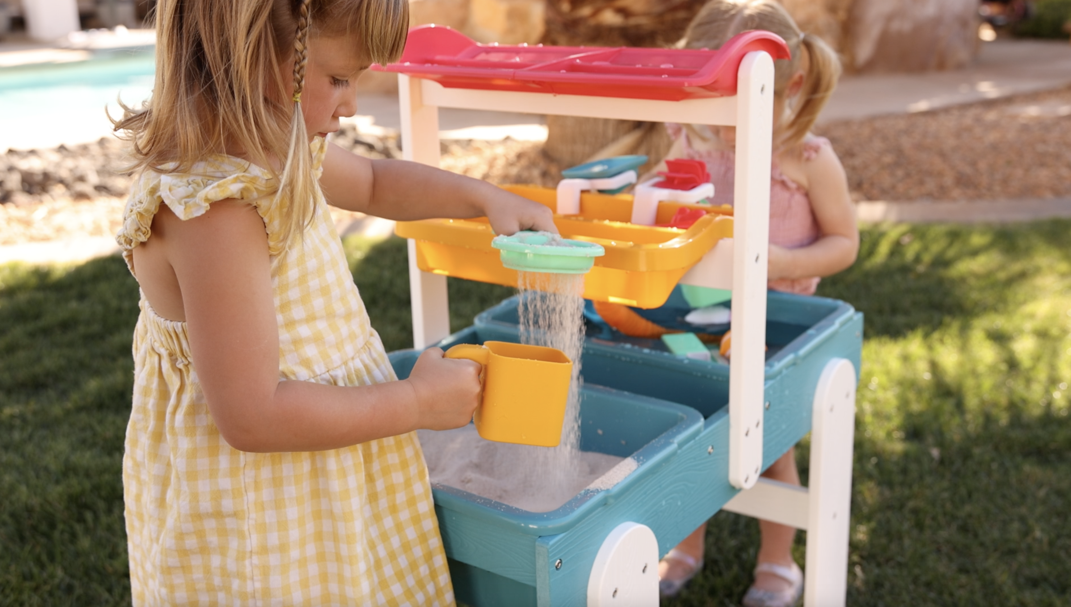 A baby wearing a bow headband sits in a white activity center, playing with a colorful toy.