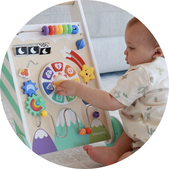 A baby sits on the floor playing with a colorful wooden activity walker.