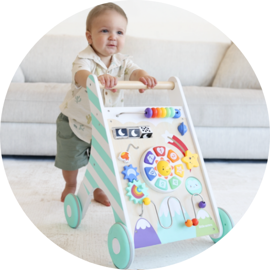 A baby stands holding onto a colorful wooden activity walker in a living room.