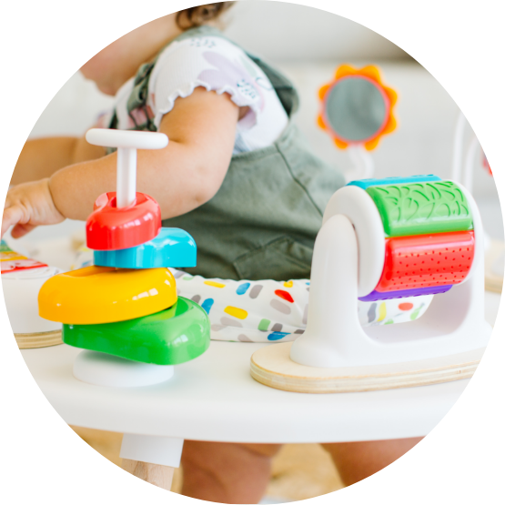 A close-up of a baby in a high chair playing with colorful stacking rings and other toys.