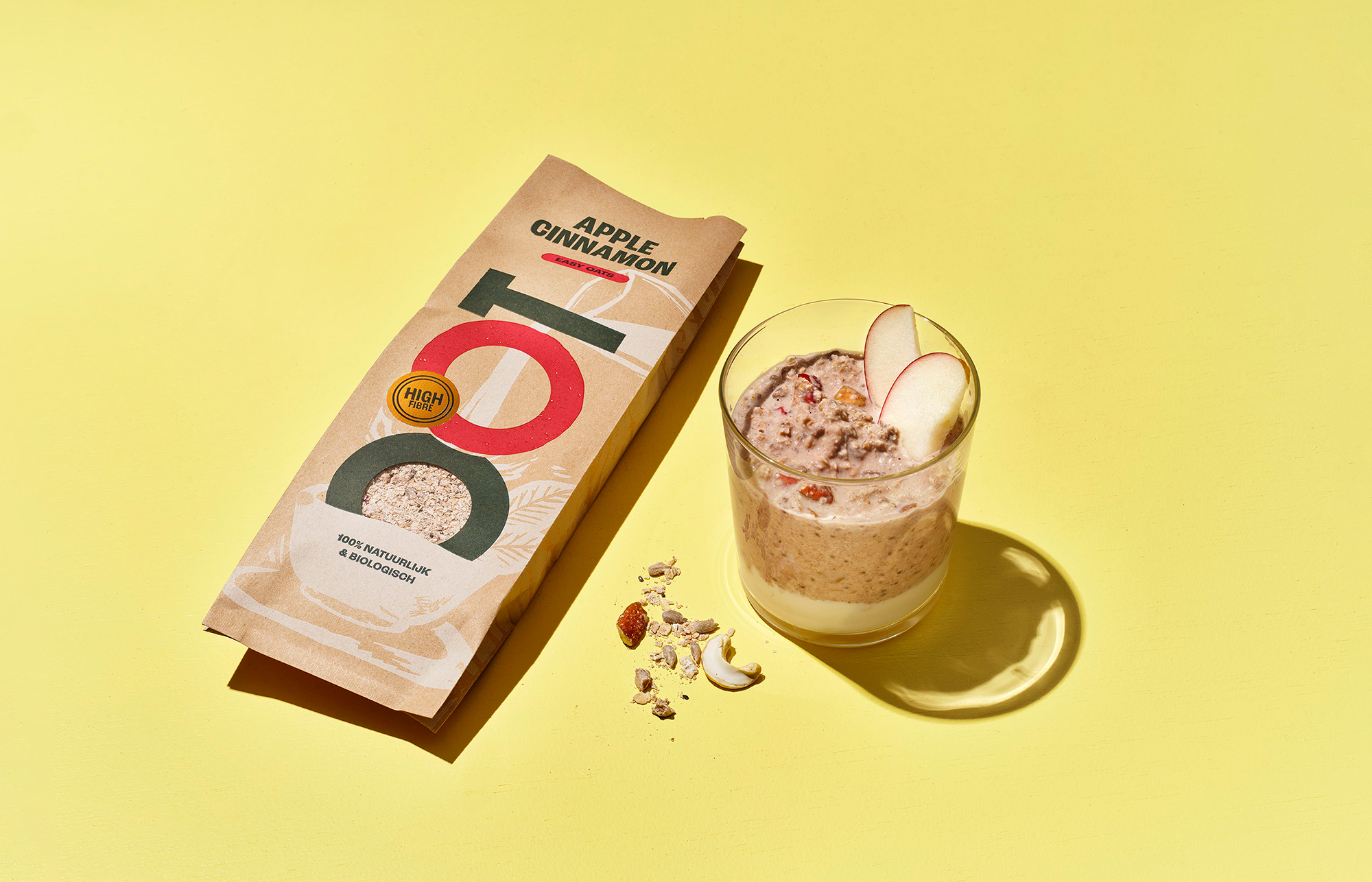 Apple cinnamon oatmeal packet and glass with oats on yellow background.