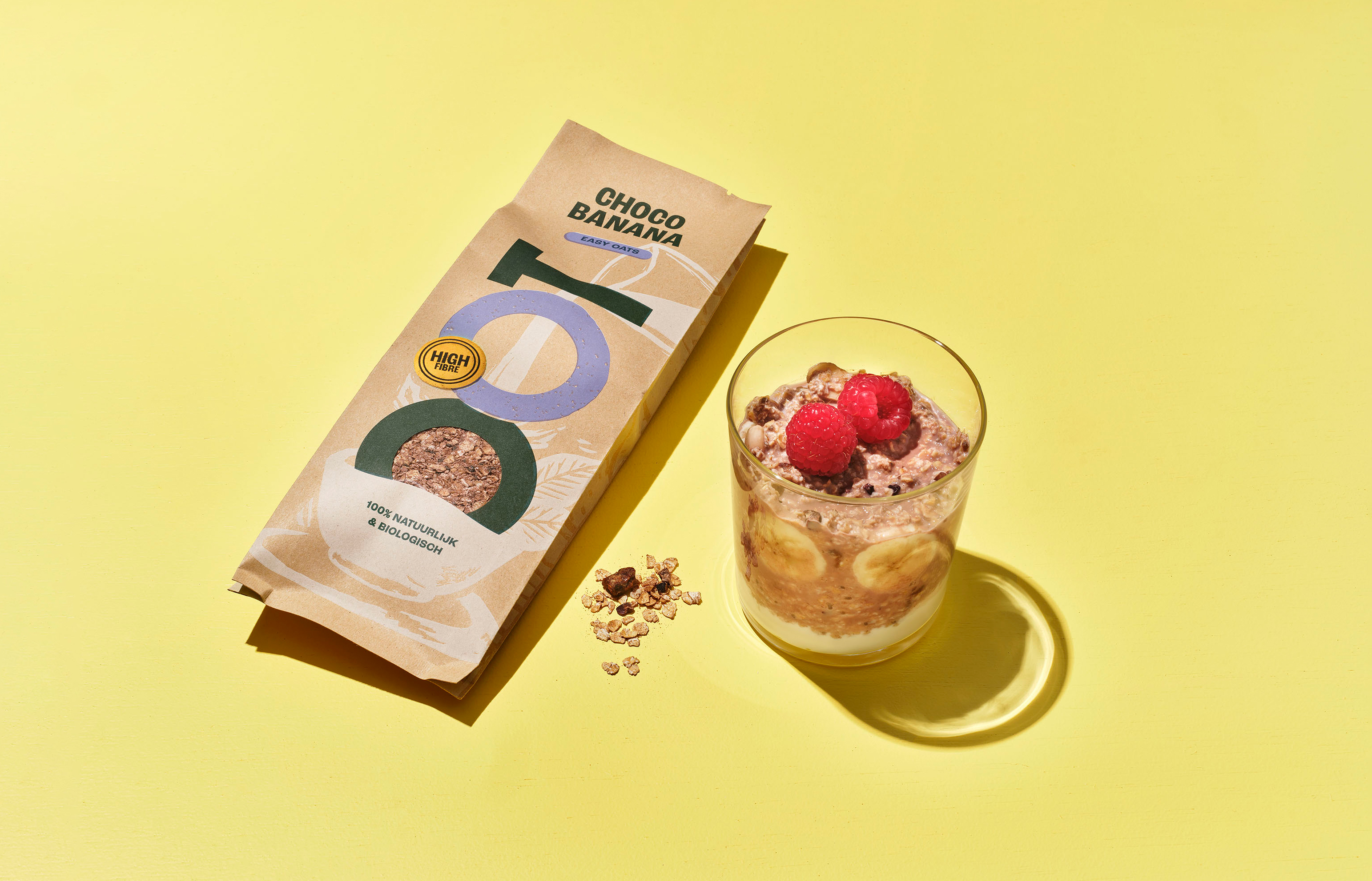 Choco banana oats package and glass with oats, banana, raspberries on yellow background.