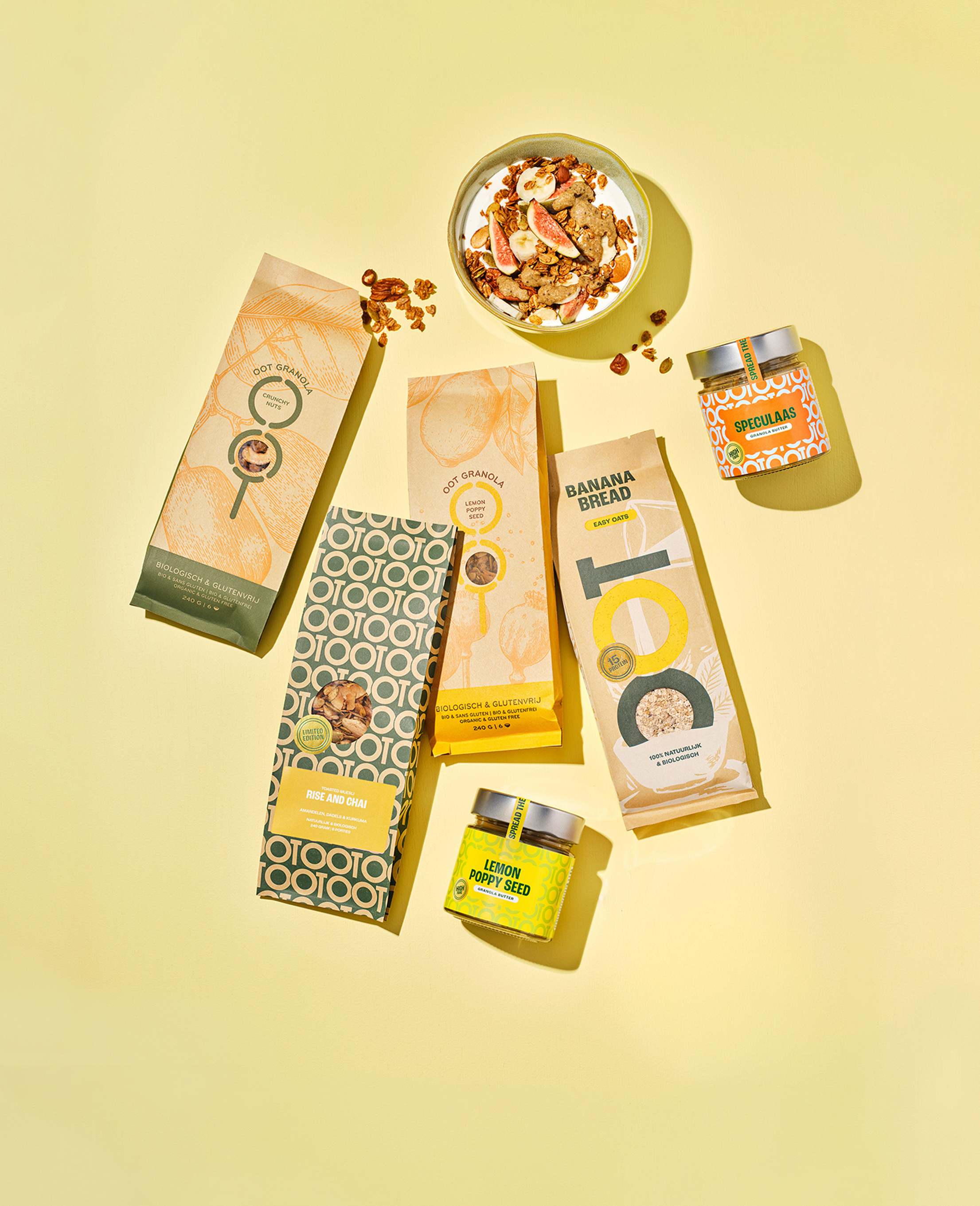 An overhead view of various granola products, jars of spread, and a bowl of yogurt on a yellow background.