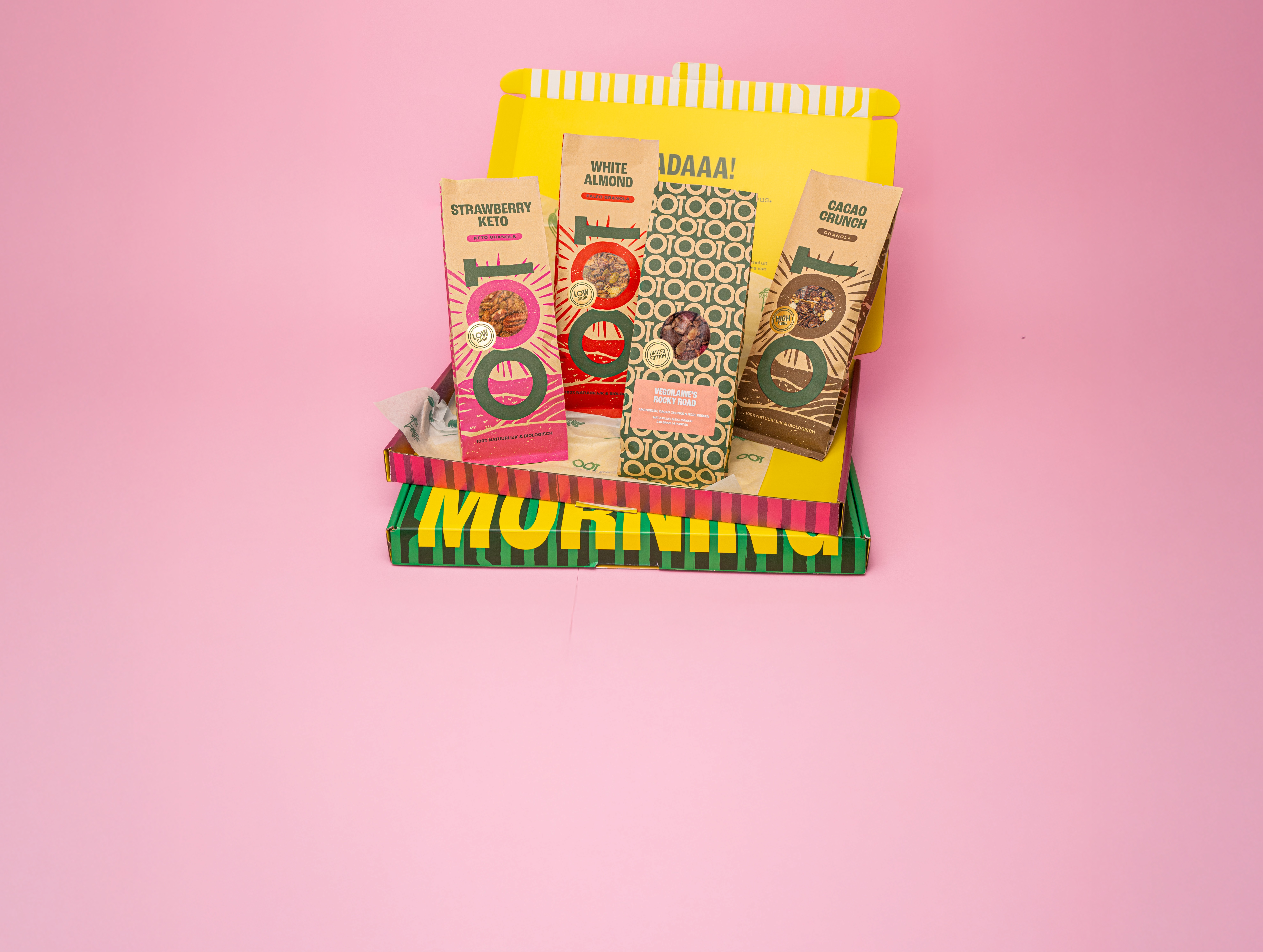 Several bags of granola inside a colorful box set against a pink background.