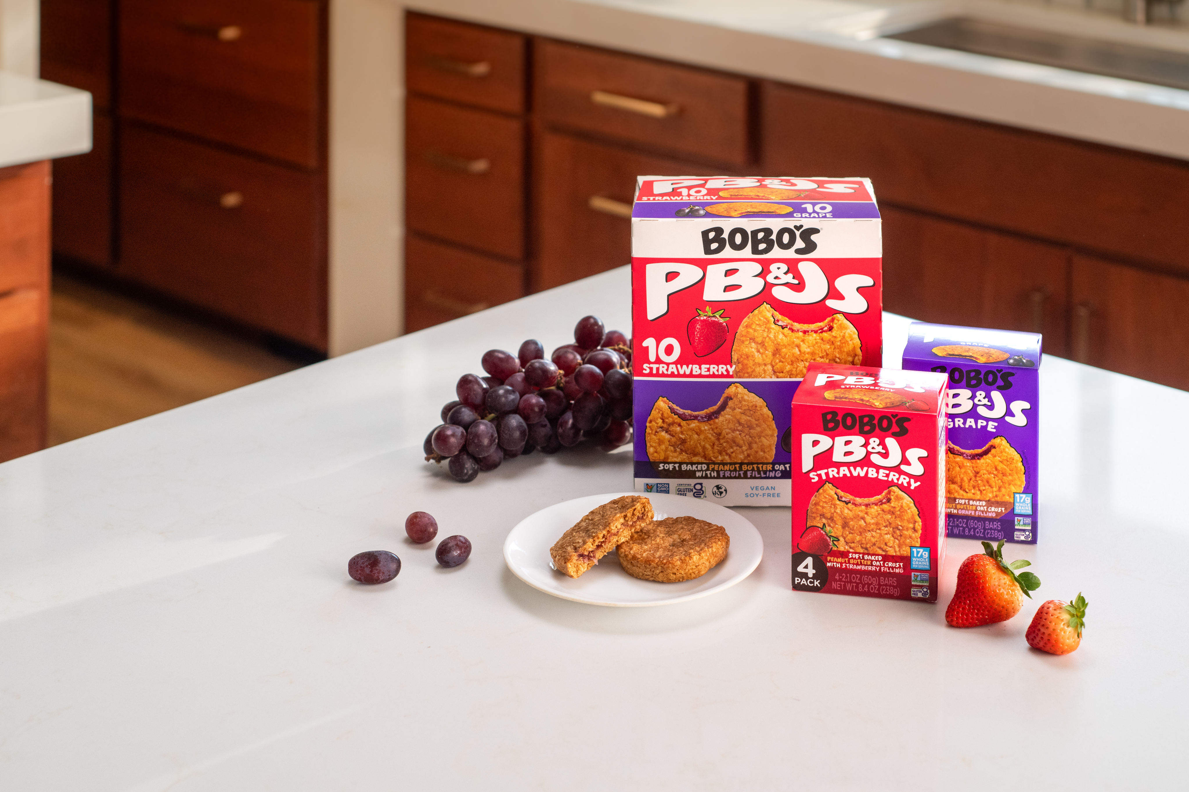 Boxes of Bobo's PB&J snacks with grapes and strawberries on a kitchen counter.