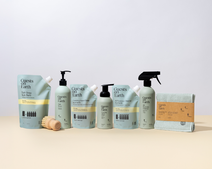 A collection of Guests on Earth cleaning products, including refill pouches, bottles, a brush, and a cloth.