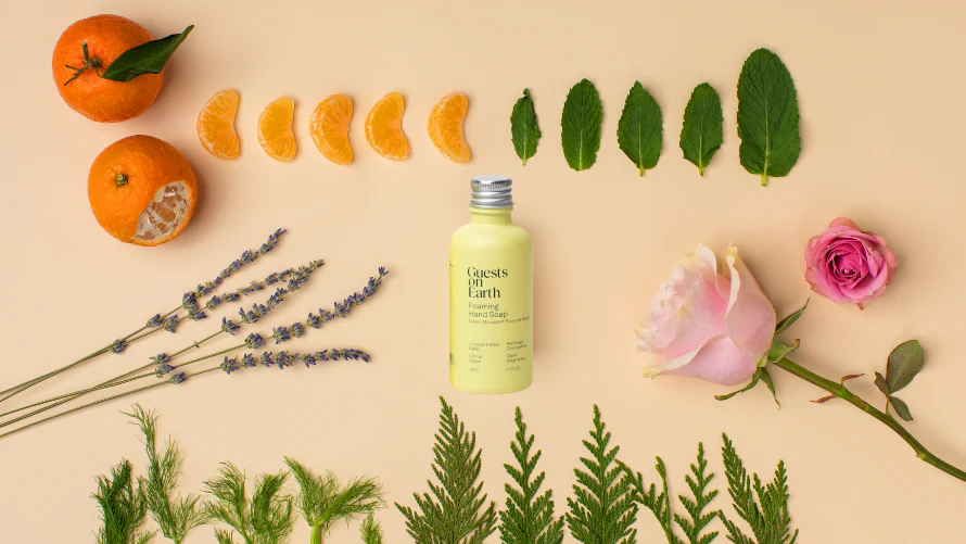 A bottle of hand soap in a flat lay with its ingredients: tangerine, mint, lavender, and roses.