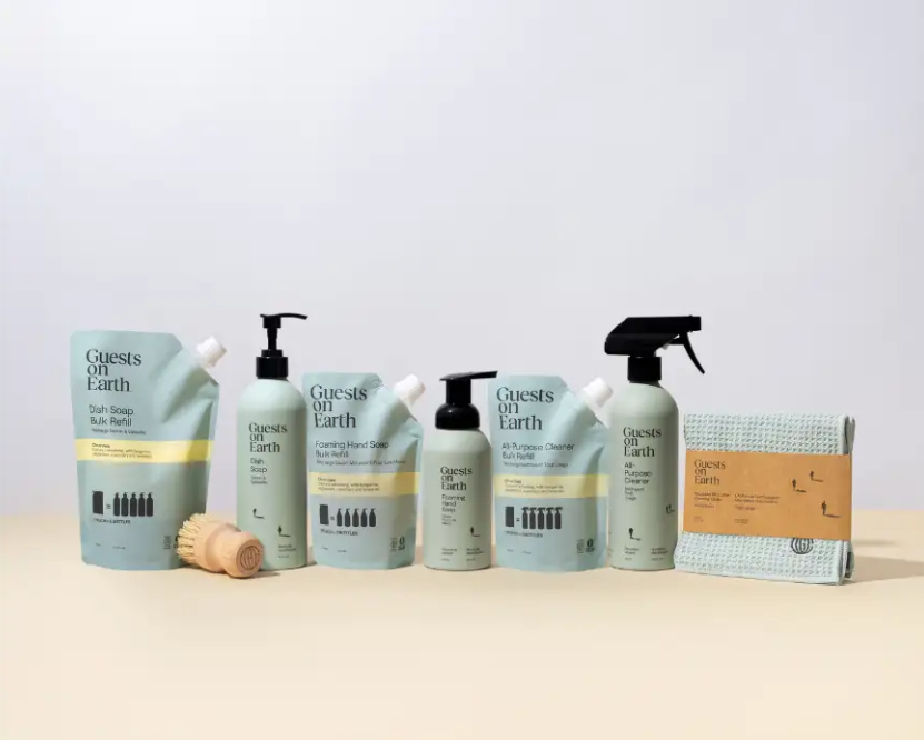 A lineup of Guests on Earth cleaning products including bottles, refill pouches, a brush, and a cloth.