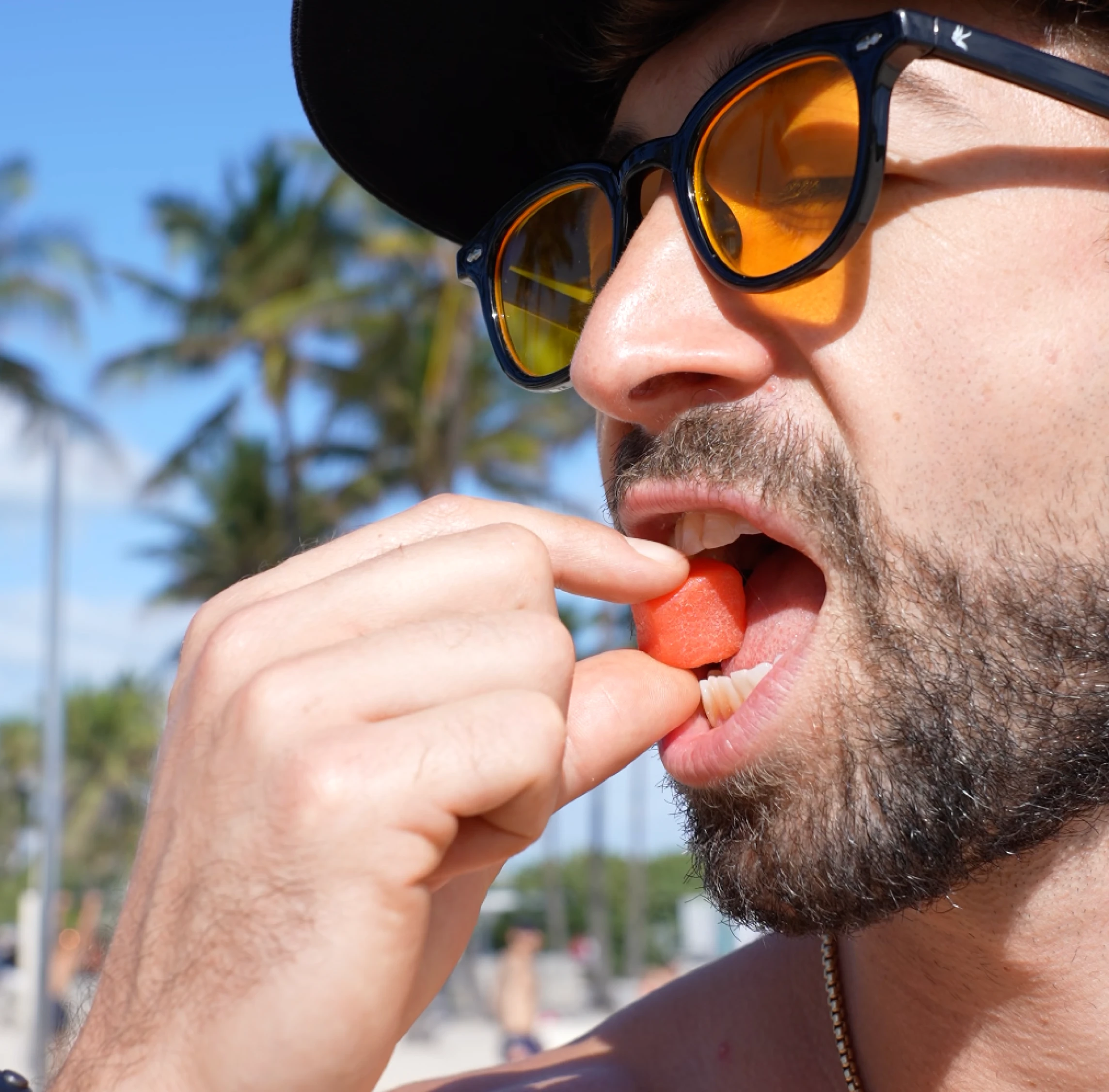 Person wearing sunglasses eating a piece of watermelon outdoors.