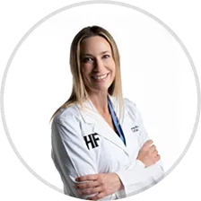 A smiling person in a white lab coat with folded arms.