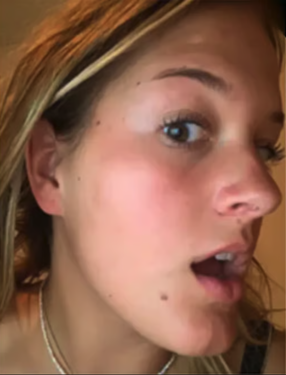 A close-up, side profile of a young woman with blonde hair and her mouth open in surprise.