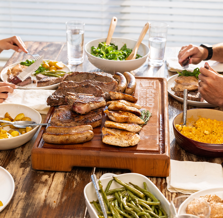A table set with various meats, sides, and hands reaching for food.