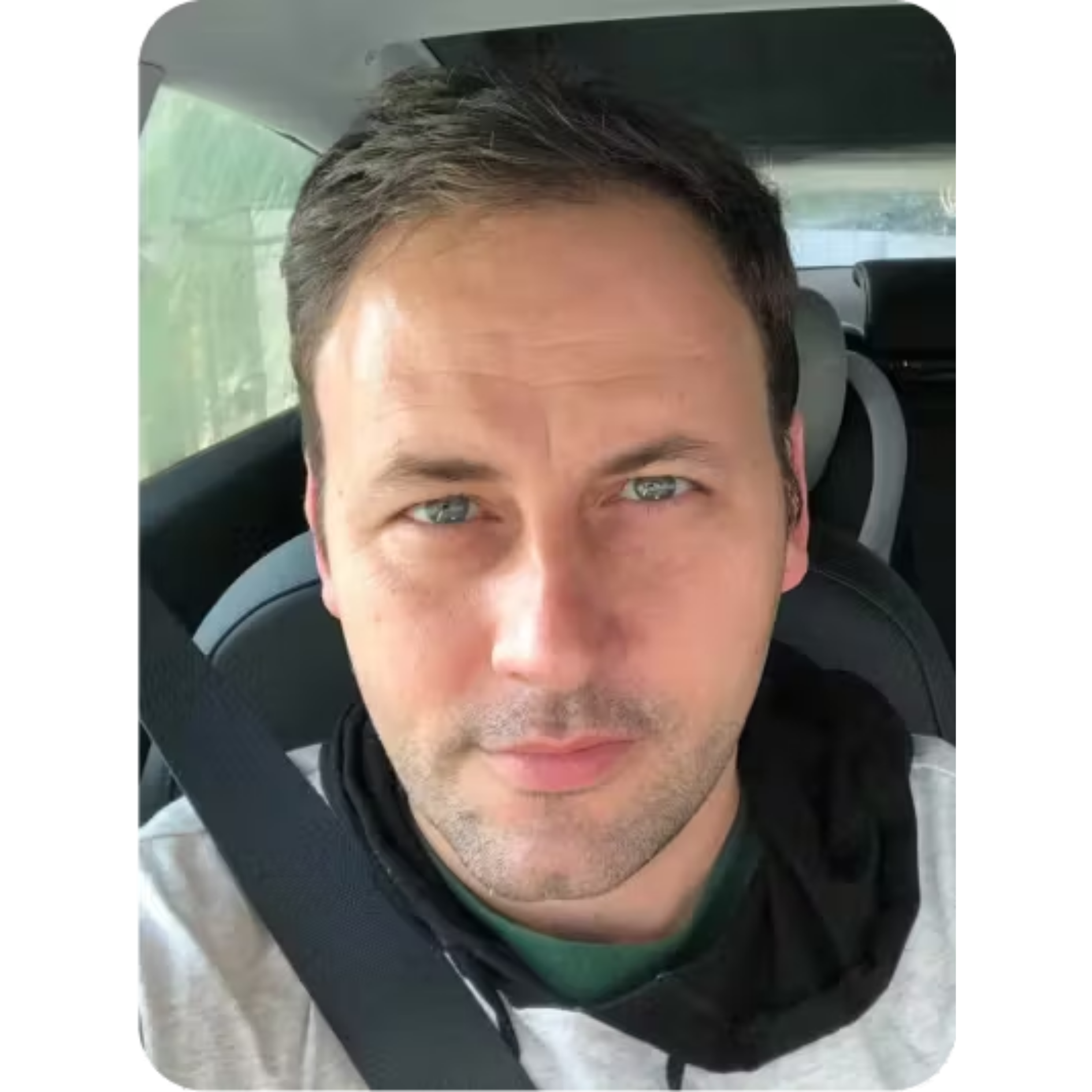 Person sitting in a car, wearing a seatbelt, looking at the camera.