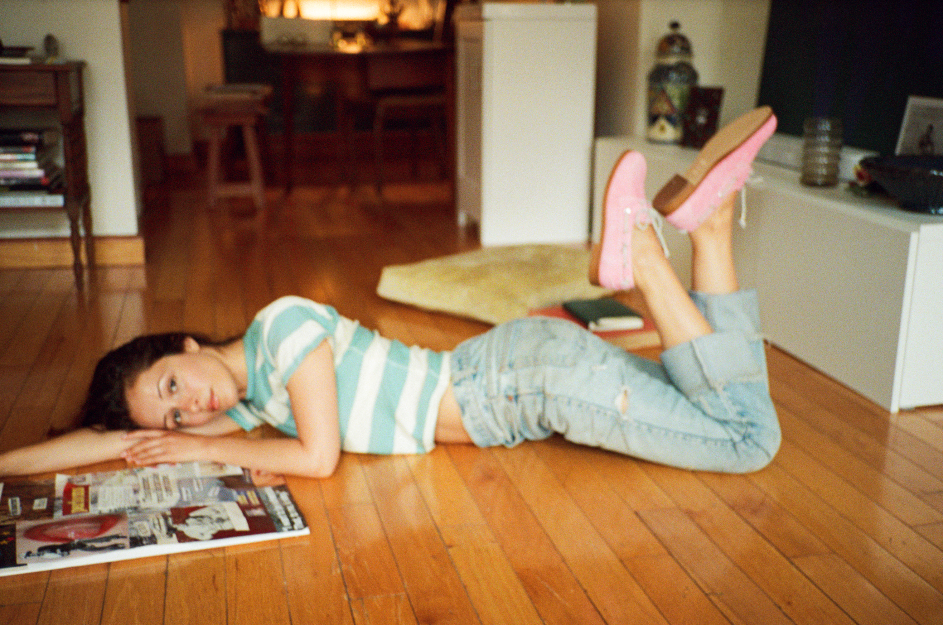 Person lying on wooden floor, wearing striped shirt and jeans, with pink shoes.