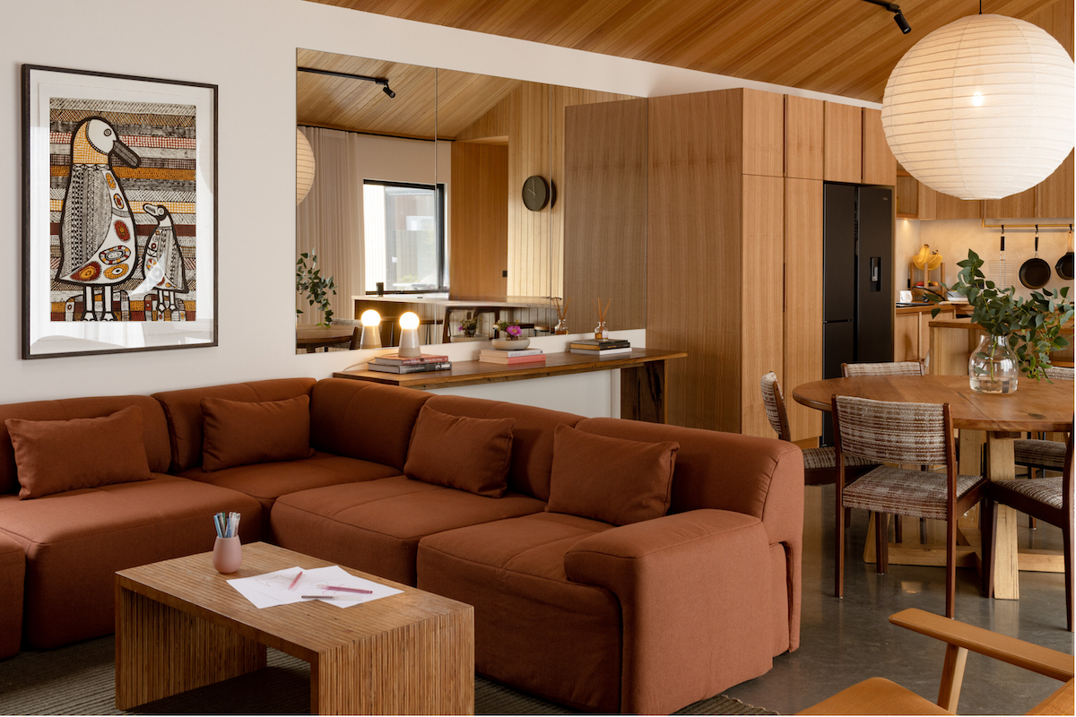 A modern, open-plan living space with a rust-colored sofa, wood paneling, and a dining area.