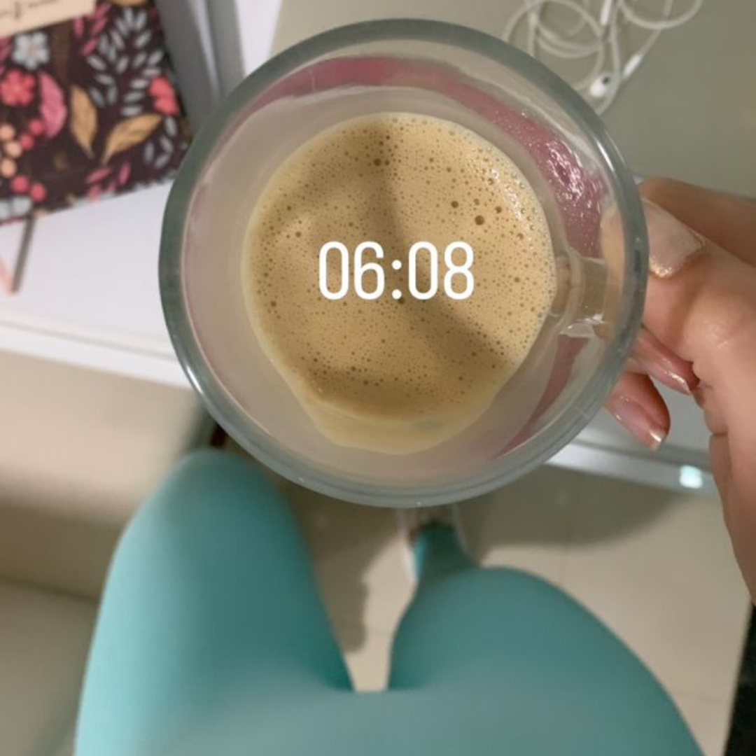 A hand holding a frothy coffee cup with the time 06:08 displayed.