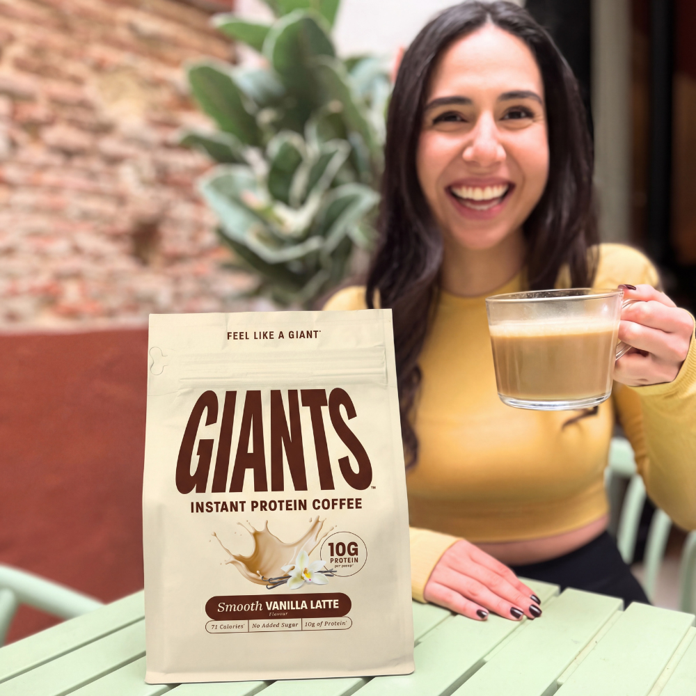 Woman holding coffee cup beside a bag of Giants instant protein coffee.