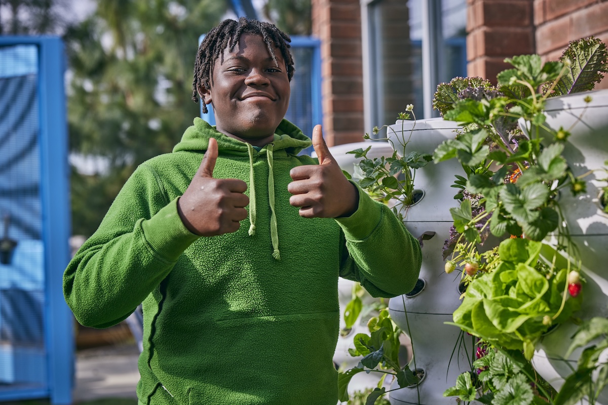 Person in green hoodie giving thumbs up near vertical garden.