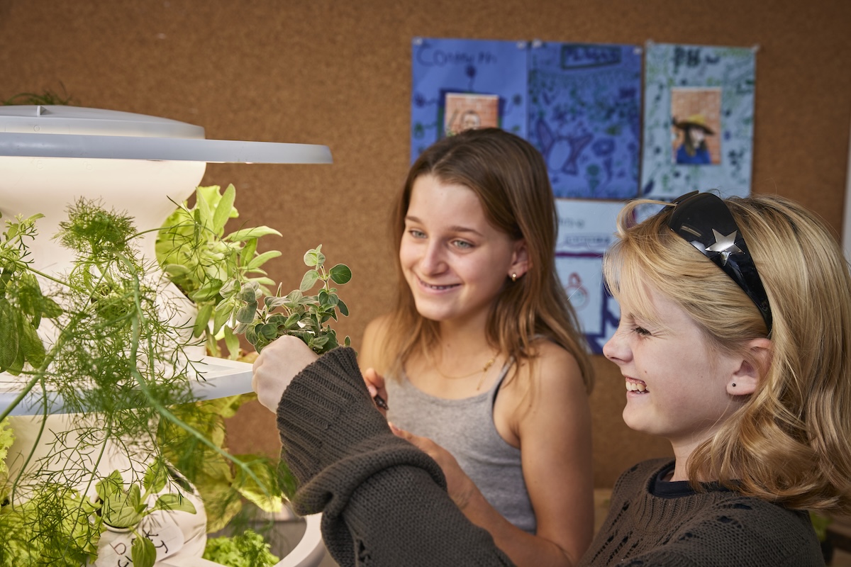 Two children smiling and examining plants indoors.