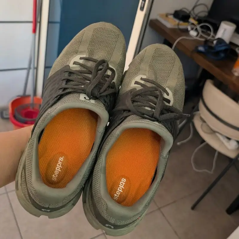 A pair of gray athletic shoes with bright orange insoles being held up for the camera.