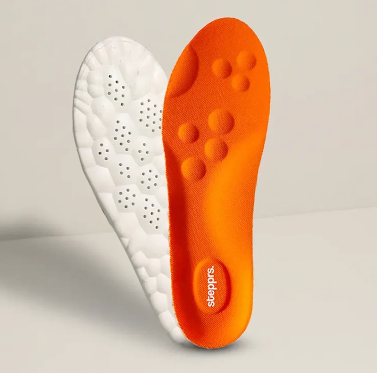 Two shoe insoles, one orange and one white with perforations, are displayed upright.