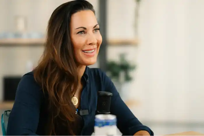 Woman smiling and speaking into a microphone indoors.