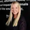 Person with long blonde hair smiling in front of a text-covered wall.