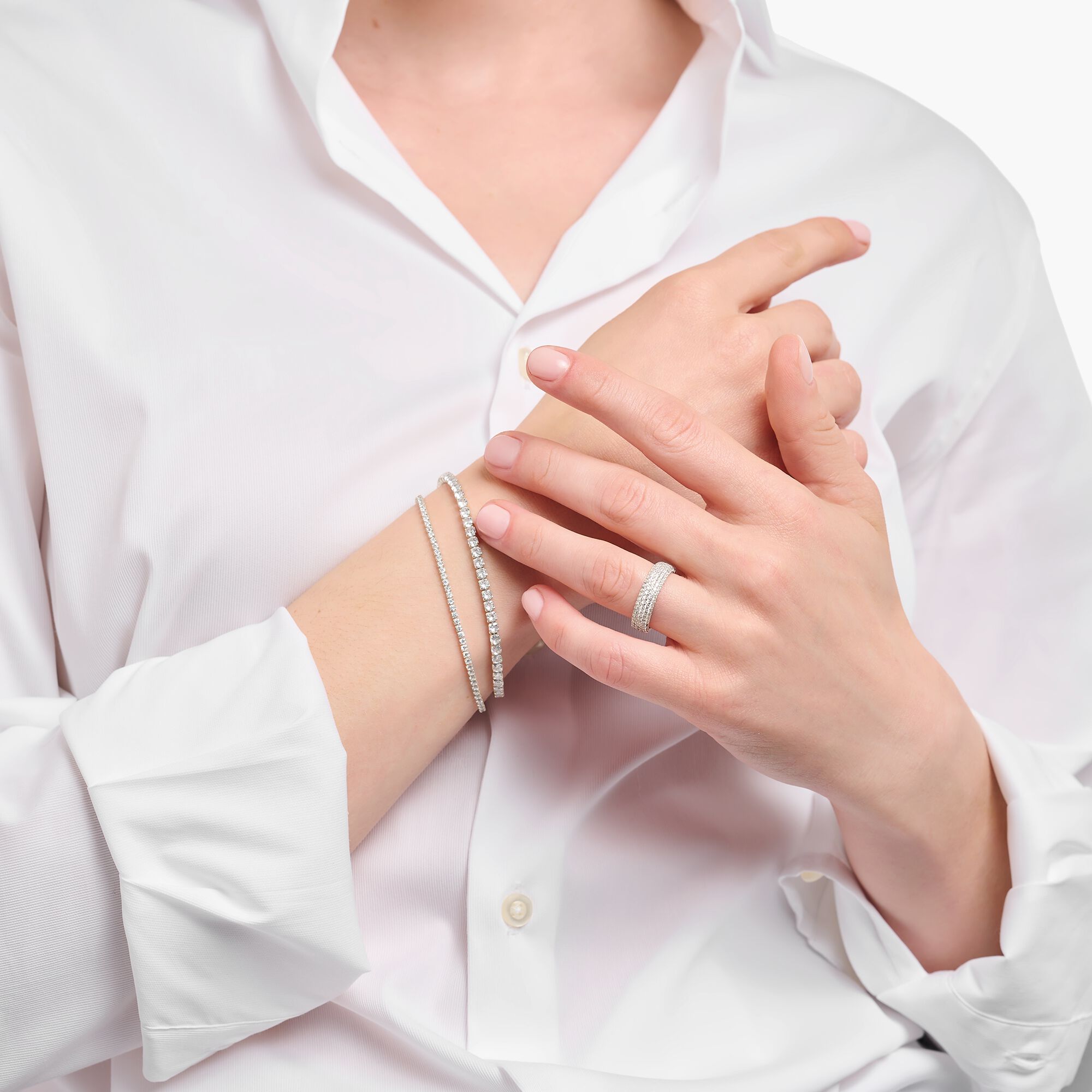 Person wearing a white shirt, showcasing bracelets and a ring on their hands.