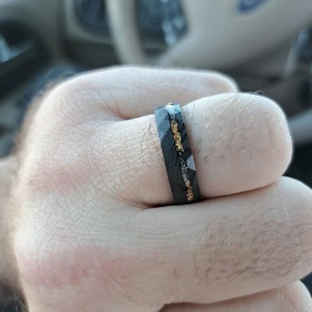 A hand wearing a dark ring with gold accents.