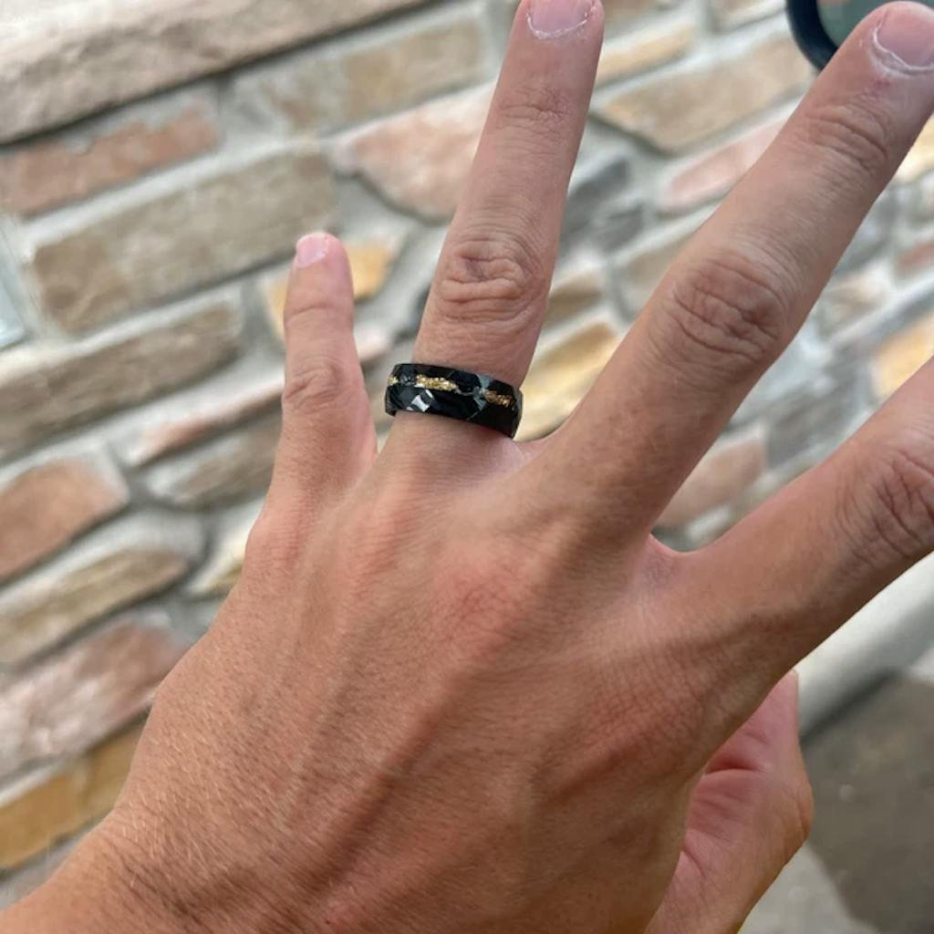 Hand with a patterned black ring, brick wall background.