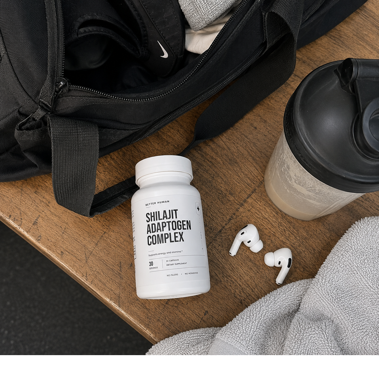 A bottle of Shilajit Adaptogen Complex supplements sits on a wooden bench with a gym bag and earbuds.