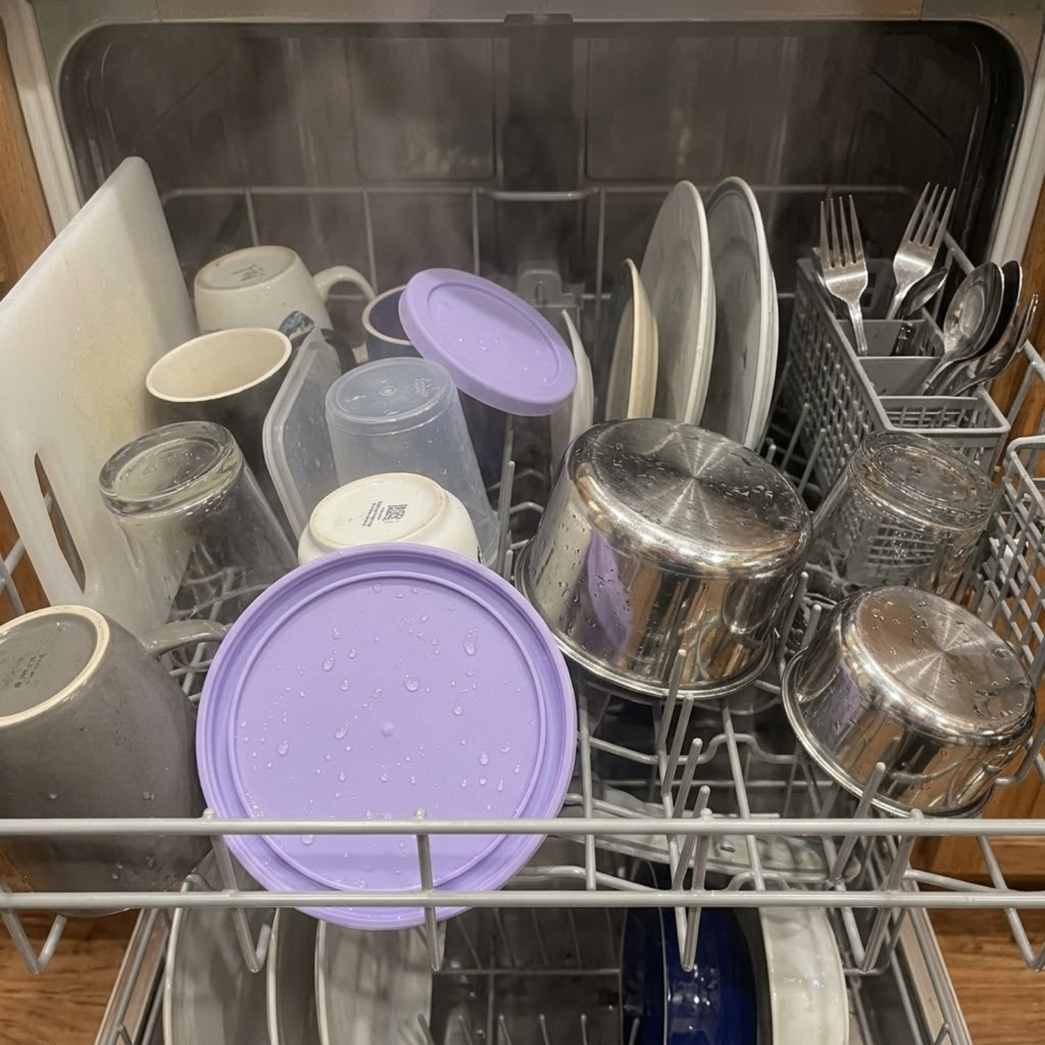 An open dishwasher filled with clean, wet dishes, pots, and utensils on the racks.